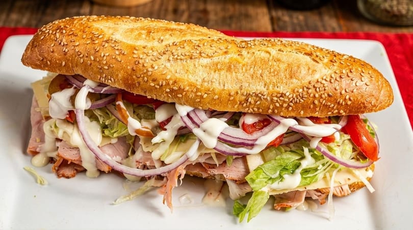 A large, sesame-seed hoagie roll filled with deli meat, cheese, lettuce, red onion, tomatoes, and mayonnaise.
