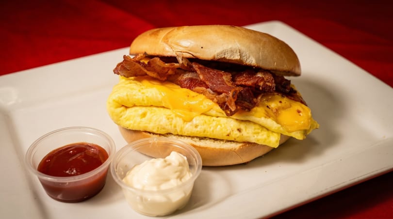 Breakfast sandwich with scrambled eggs, cheese, and bacon on a bagel, with ketchup and mayonnaise.