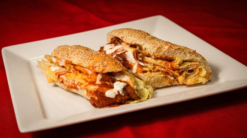 Two loaded subs with red sauce, white sauce, and cheese on a white plate.